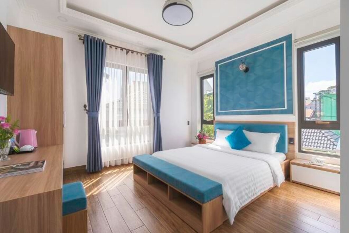 Una camera da letto moderna con pavimento in legno, un letto con lenzuola blu, un comodino, una finestra con vista e una scrivania con sedia.