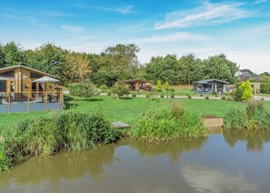 A lakeside property with wooden cabins, a grassy lawn, and a pond.