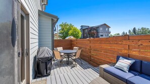 A patio with a table and chairs, a covered grill, and a blue sofa. - The 1st Street Retreat (Whitefish)