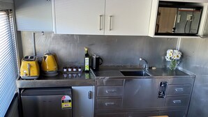 A compact kitchen with stainless steel appliances, a wooden table with a jar of granola and strawberries, and a yellow toaster.