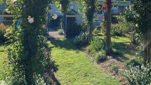 A garden with a wooden pergola structure, surrounded by lush greenery and white flowers.