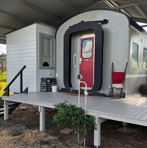 A stationary train car with a red door, a small window, and a white exterior. - A unique sleeper train carriage near Bathurst that's off the rails!
(Perthville)