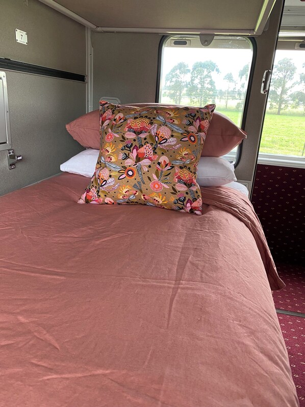 Ein Bett mit einem blumigen Kopfkissen und einer rosa Tagesdecke in einem Zimmer mit Fenster.