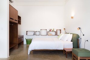 A bedroom with a bed, a green chair, a wooden wardrobe, and wall-mounted shelves with various items.
