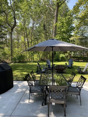 Relax in a serene garden setting, surrounded by lush greenery and a shaded patio with a grill for outdoor cooking.