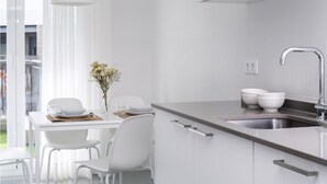 A modern kitchen with white cabinetry, a stainless steel sink, and a dining area with white chairs and a table. - Misterhost La Florida Pool & Private Terrace (Sevilla)