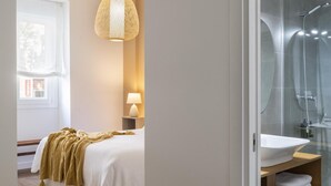 A modern bedroom with a bed, a bedside lamp, and a view of a bathroom with a shower and sink. - Misterhost La Florida Pool & Private Terrace (Sevilla)