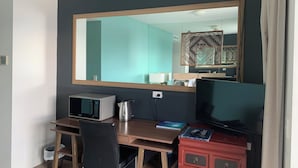 A hotel room with a large mirror, a desk with a microwave, a coffee maker, a chair, a TV, and a bookshelf.