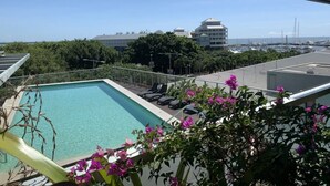 A rooftop pool with lounge chairs, surrounded by greenery and overlooking a marina with boats.