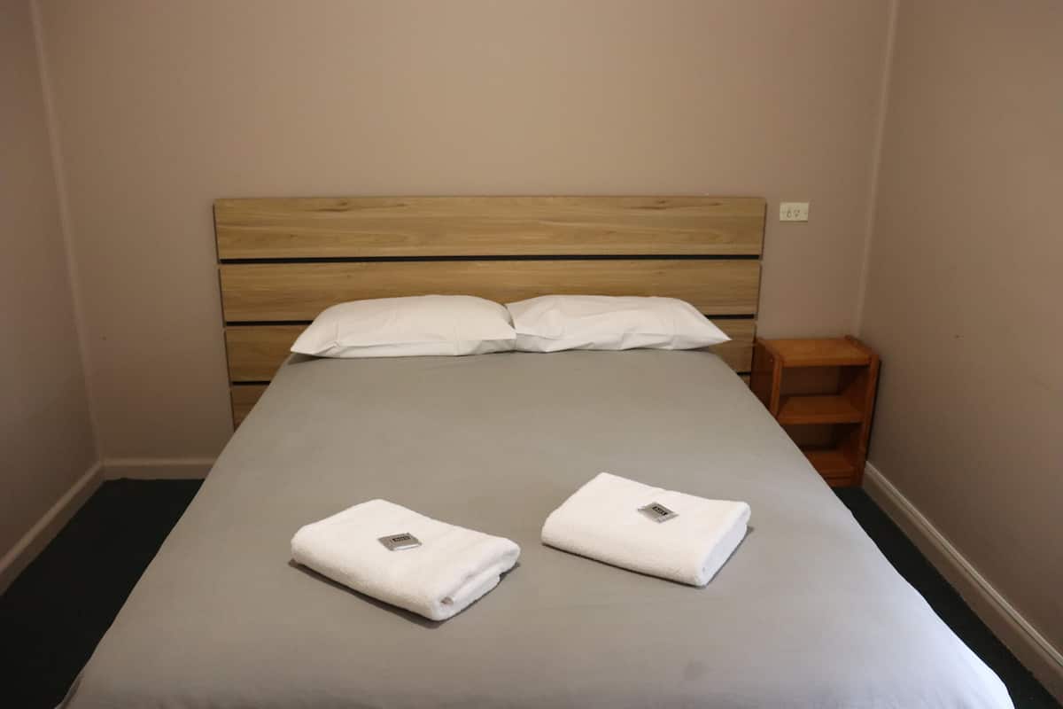A neatly made bed with a wooden headboard, two white pillows, and two folded white towels on the bed.