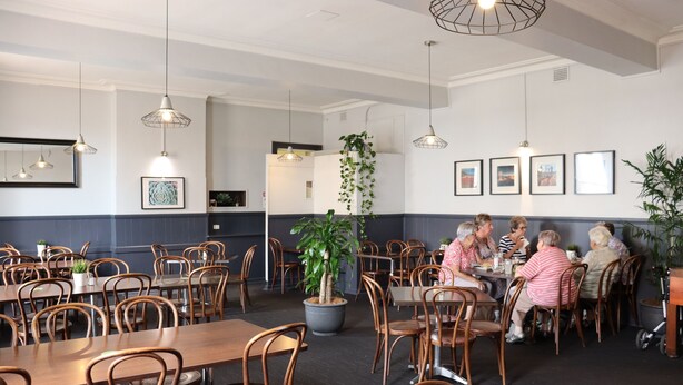 A dining area with wooden tables and chairs, hanging pendant lights, and framed pictures on the wall. - The Court House Hotel (Gunnedah)