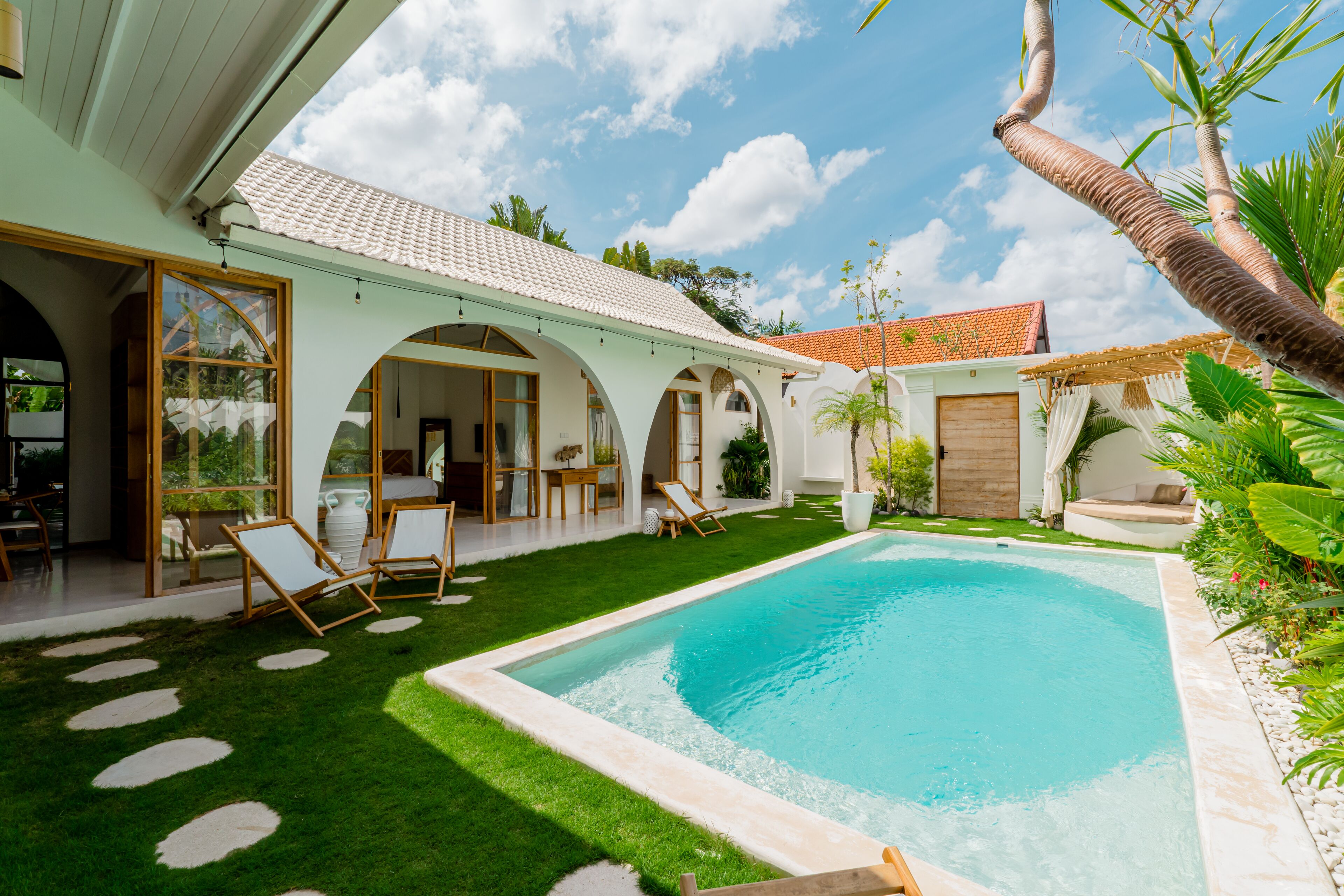 A poolside area with a clear blue pool, a grassy lawn, and a covered patio with seating.