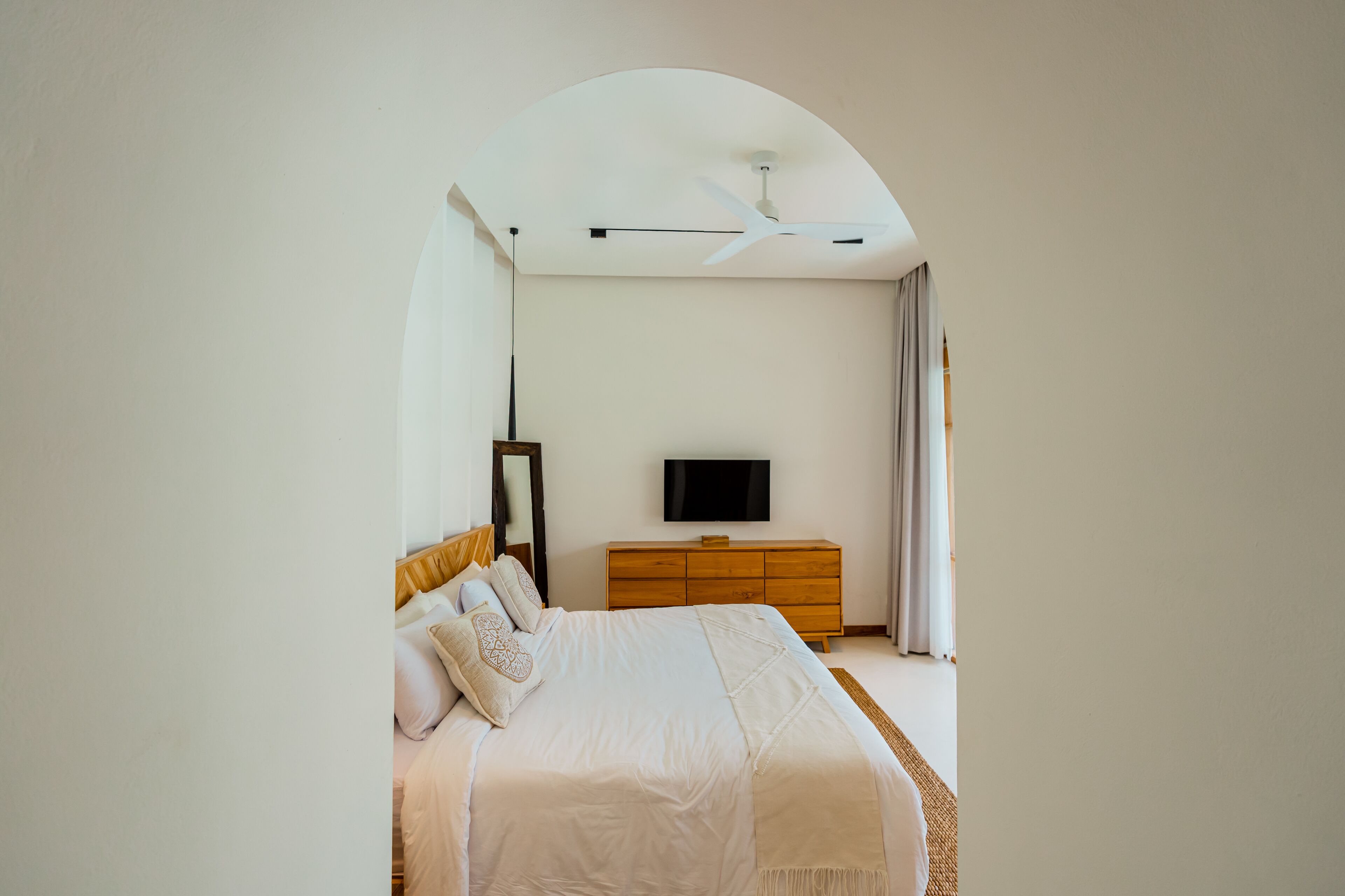 A bedroom with a bed, a wooden dresser, a flat-screen TV, and a ceiling fan.