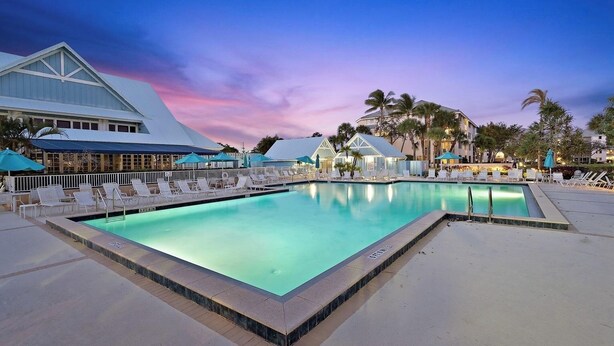 A swimming pool with lounge chairs and umbrellas, surrounded by palm trees and buildings. - Jupiter Bay Resort Condo, steps to the beach! Comfortably sleeps family of 4! (Jupiter)