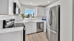 A modern kitchen with white cabinetry, stainless steel appliances, and a window providing natural light. - Jupiter Bay Resort Condo, steps to the beach! Comfortably sleeps family of 4! (Jupiter)