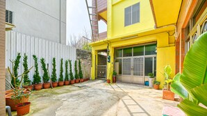 A courtyard with potted plants, a concrete floor, and a yellow building with a large window and door. - Chunfa B&B (Huxi)
