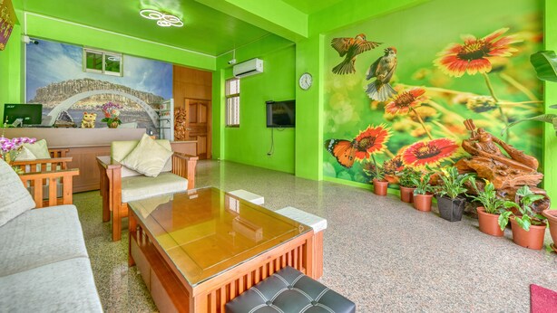 A room with a green wall, a wooden sofa, a glass-top table, and a mural of birds and flowers. - Chunfa B&B (Huxi)