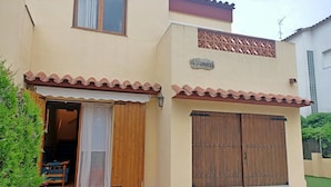 A two-story building with a beige facade, a wooden door, and a tiled patio. - Summer house close to the forest in L'Escala.HUTG-071512 (l'Escala)