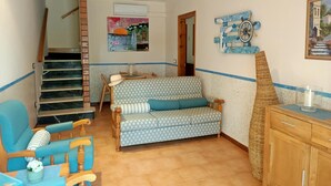 A cozy living room with a patterned sofa, a wooden chair, a small table with a hat, and a decorative wall piece. - Summer house close to the forest in L'Escala.HUTG-071512 (l'Escala)