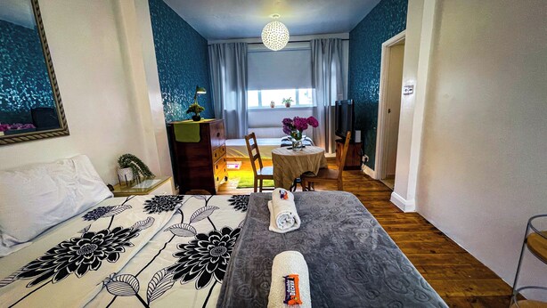 Hotellihuone, jossa on sänky, työpöytä, tuoli, kukkia koristeltu pöytä ja ikkuna, jossa on verhot.