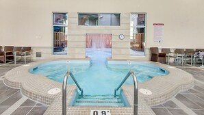 En indendørs swimmingpool med fliseterrasse, et ur og et skilt vedrørende regler for spabad.