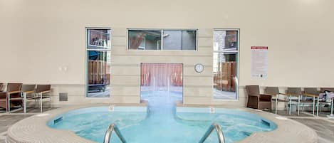 Piscina interior com deck revestido, um relógio e um aviso sobre as regras da hidromassagem.