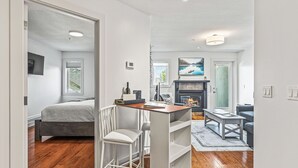Ein modernes Wohnzimmer mit Kamin, ein Essbereich mit Tisch und Stühlen sowie ein Schlafzimmer mit Bett und Fenster.