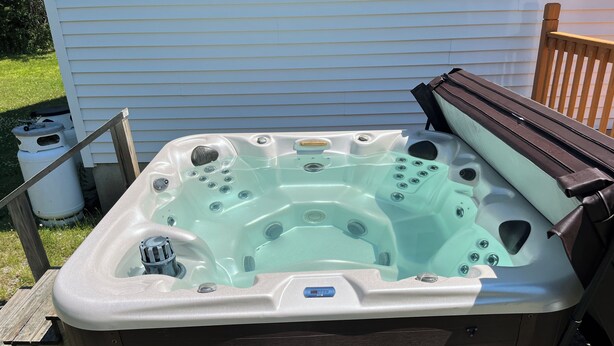 Ein Whirlpool mit Bedienfeld, eine Holzterrasse und ein weißes Haus im Hintergrund.