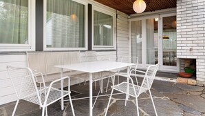 Een terras met een witte tafel en stoelen, een metselwerk schoorsteen en een houten plafond.