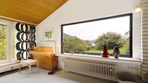Een moderne kamer met een piano, een radiator, een raam met uitzicht en een stoel.