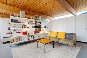 Una sala de estar moderna con techo de madera, estanterías blancas, un sofá con cojines amarillos y una mesa de centro.