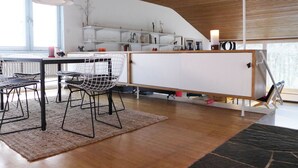 Een moderne keuken met witte kasten, een eethoek met een tafel en stoelen, en een groot raam dat zorgt voor daglicht.
