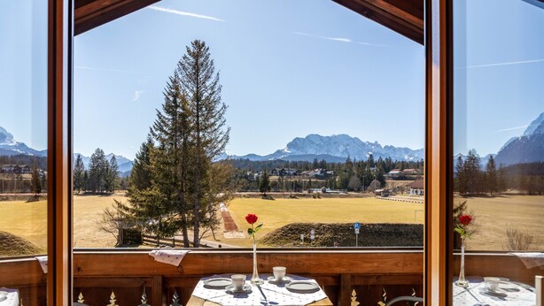 Un balcon en bois avec une table dressée pour deux personnes, offrant une vue sur un paysage montagneux.