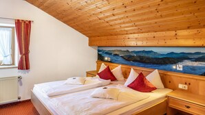 Une pièce avec un plafond en bois, un lit avec une literie blanche et des oreillers rouges, une table de chevet et un tableau représentant un paysage montagneux.