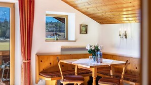 Un espace repas avec un banc en bois, une table avec un menu et une fenêtre donnant sur des maisons.