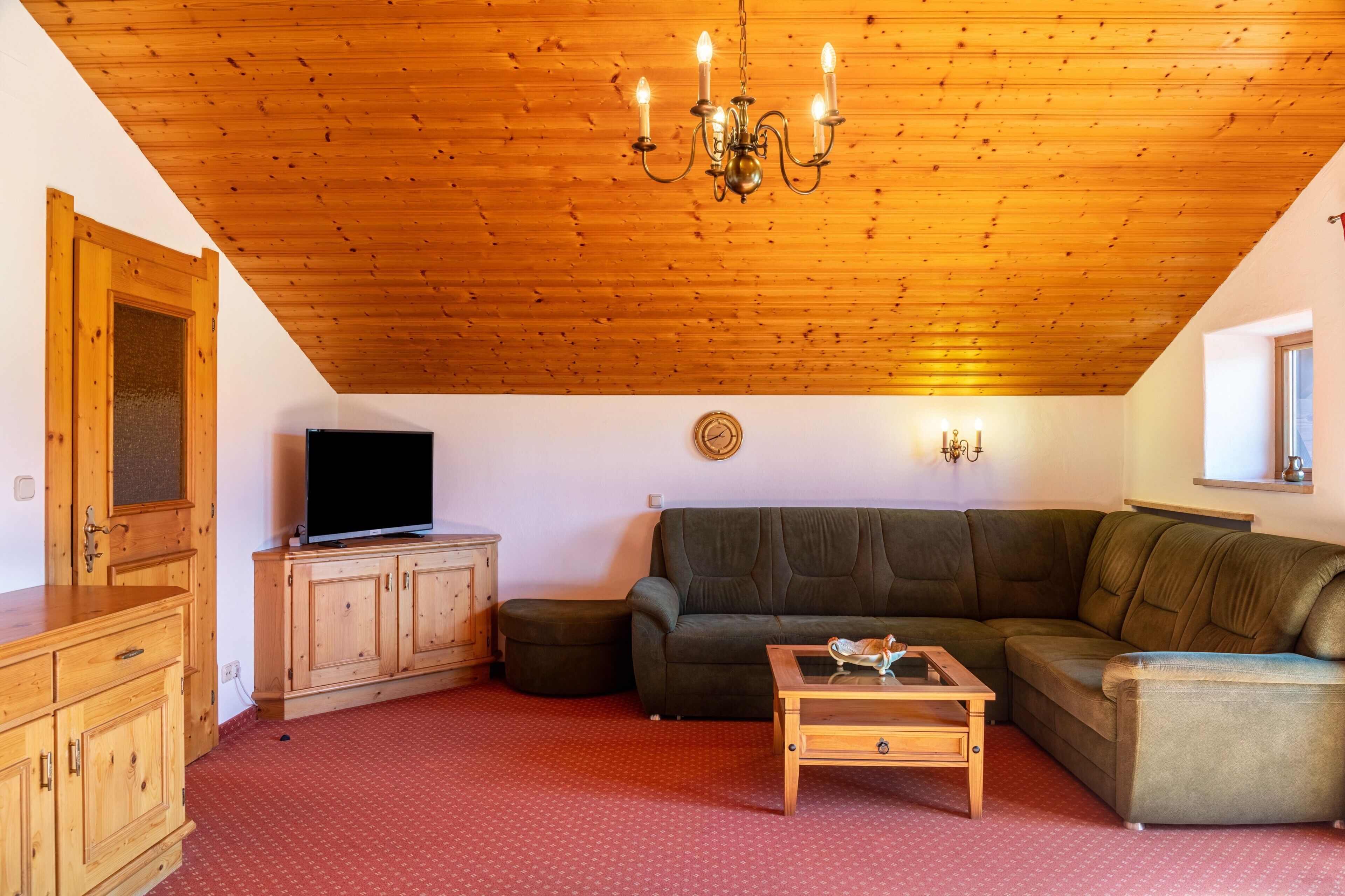 A cozy living room with a wooden ceiling, a television, a sofa, a coffee table, and a cabinet.