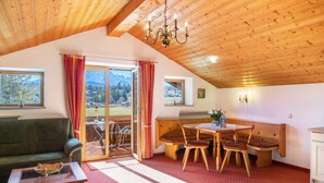 Une pièce chaleureuse avec un plafond en bois, une table à manger avec des chaises, un canapé et une table basse avec un plateau en verre.