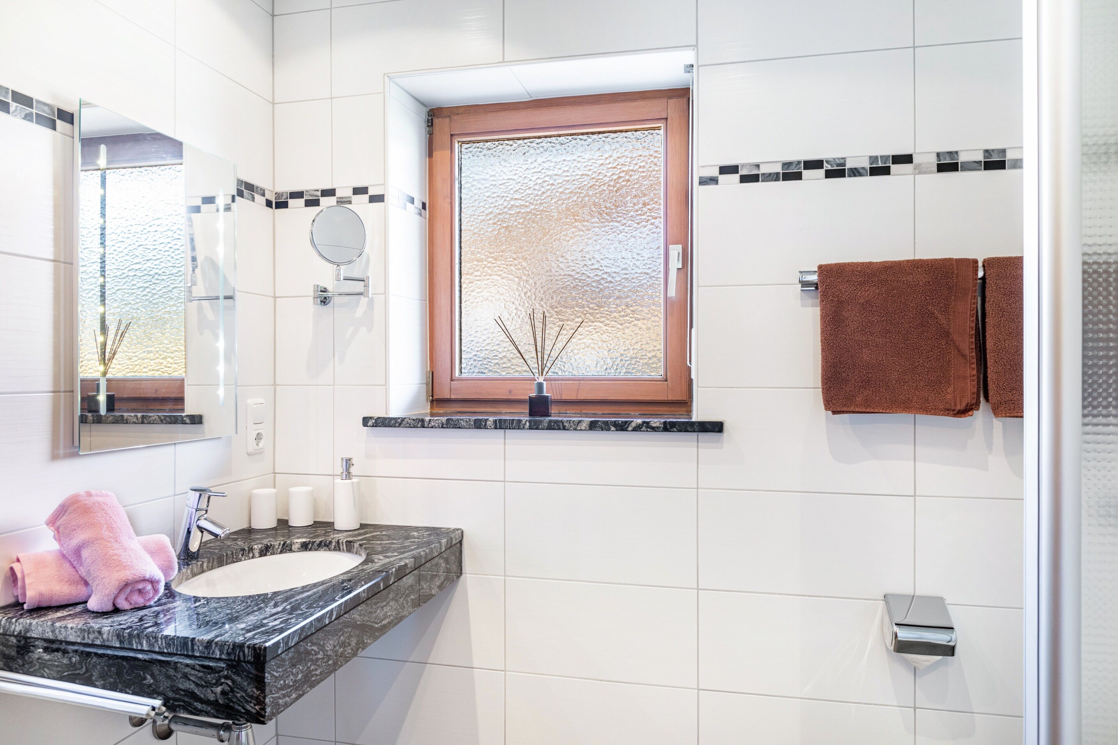 Une salle de bain avec un lavabo en marbre, un miroir, une fenêtre et deux serviettes.
