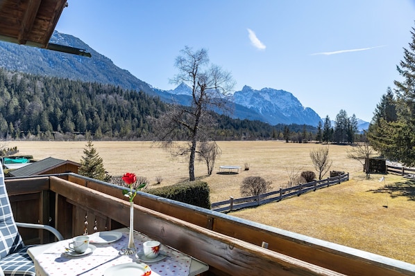 Un balcon avec une table dressée pour deux personnes, offrant une vue sur un paysage montagneux.