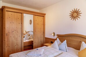 Une chambre avec une armoire en bois, un lit avec des oreillers, une table de chevet et une décoration murale représentant un soleil.