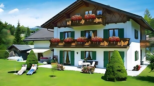 A two-story chalet with a balcony, a lawn, and a small garden.