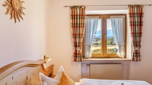 A bedroom with a wooden headboard, a bed with white bedding, a window with curtains, and a view of the outside.