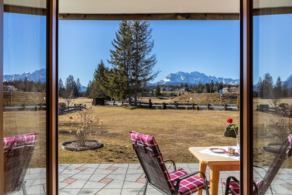A view from a room with large windows overlooking a grassy yard with a tall tree and mountains in the distance.