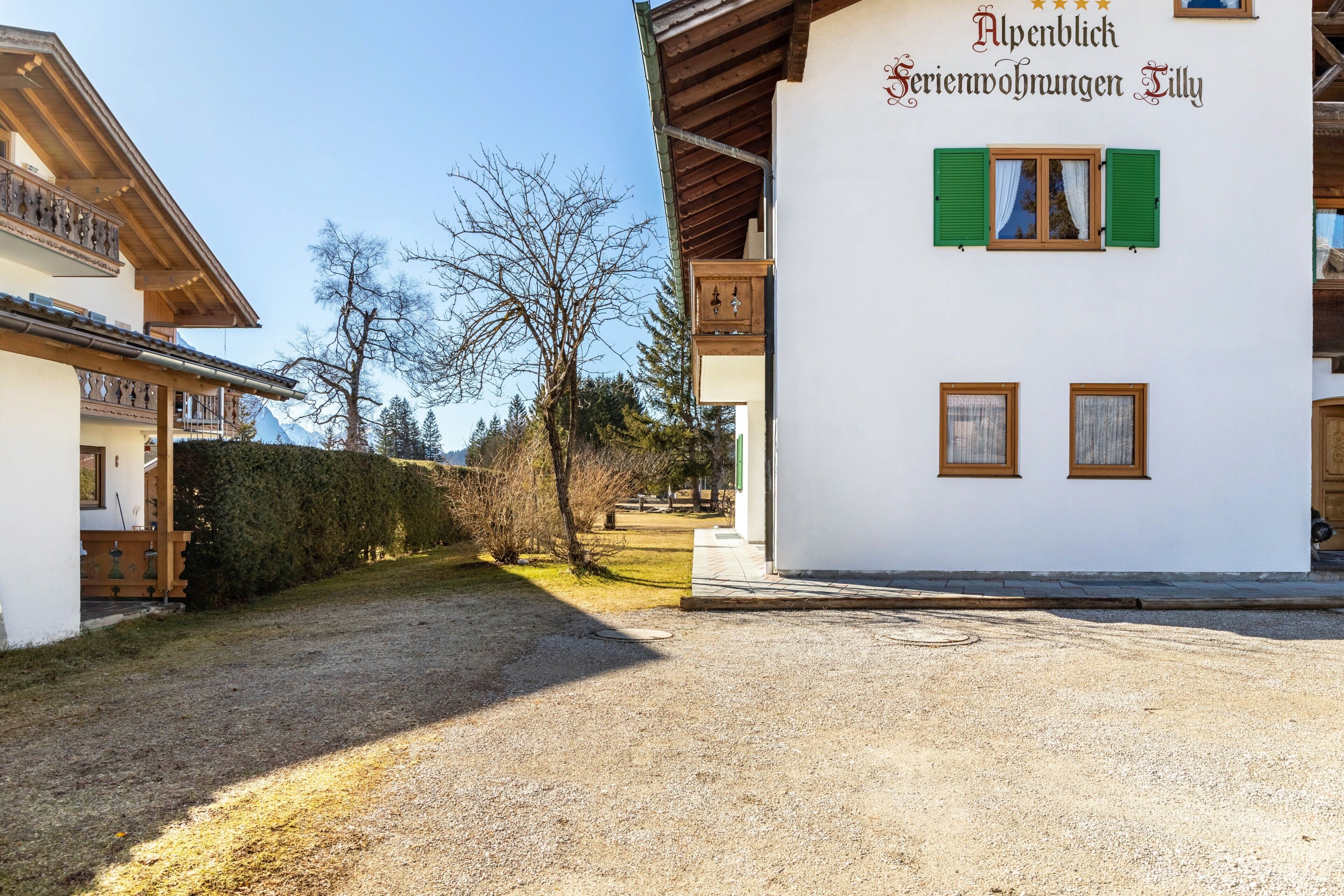Ein Gebäude mit einem Schild, auf dem 'Alpenblick Serienwohnungen Silly' steht, und einer Schotterzufahrt.