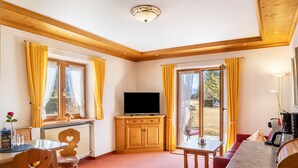 Ein Zimmer mit Fernseher, Holzschränken, einem Esstisch und einer Couch.
