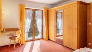 Ein Zimmer mit einem Holztisch, einem Stuhl, einem Bett und einer Schiebetür zu einem Außenbereich.