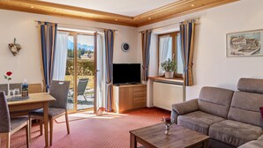 Una sala de estar con sofá, televisor, mesa de comedor con sillas y ventana con cortinas.