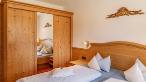 Un dormitorio con un armario de madera, una cama con ropa de cama blanca y una lámpara de pared.