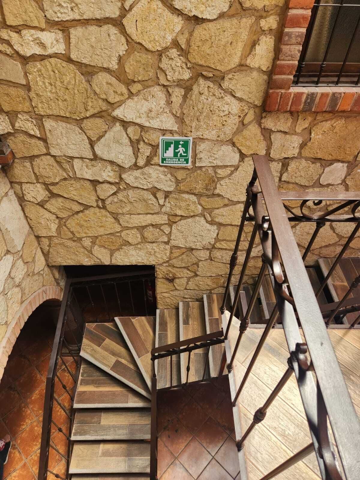 Una escalera de piedra con barandilla metálica y un letrero verde de salida de emergencia.