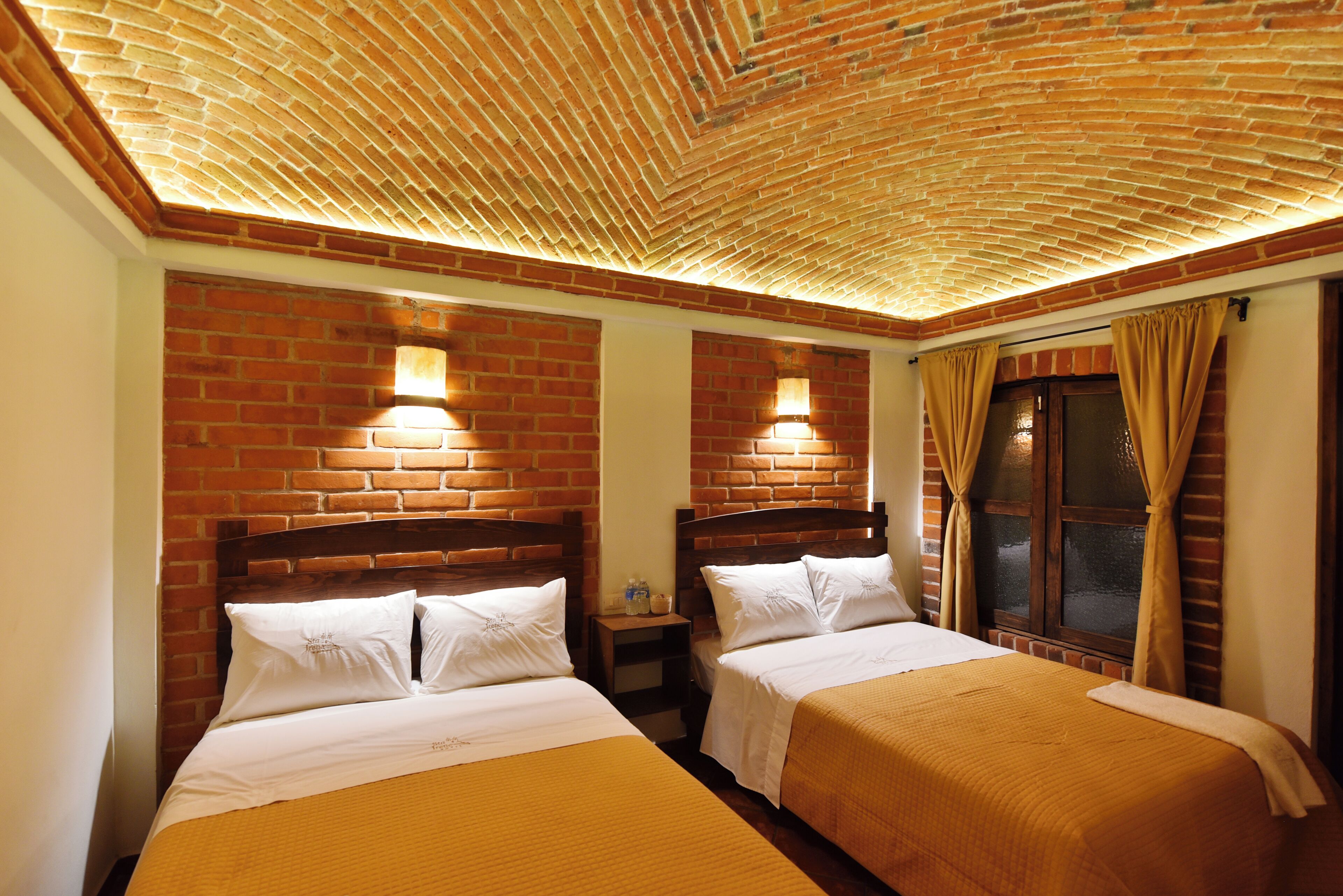Habitación de hotel con dos camas, paredes de ladrillo y techo de madera.